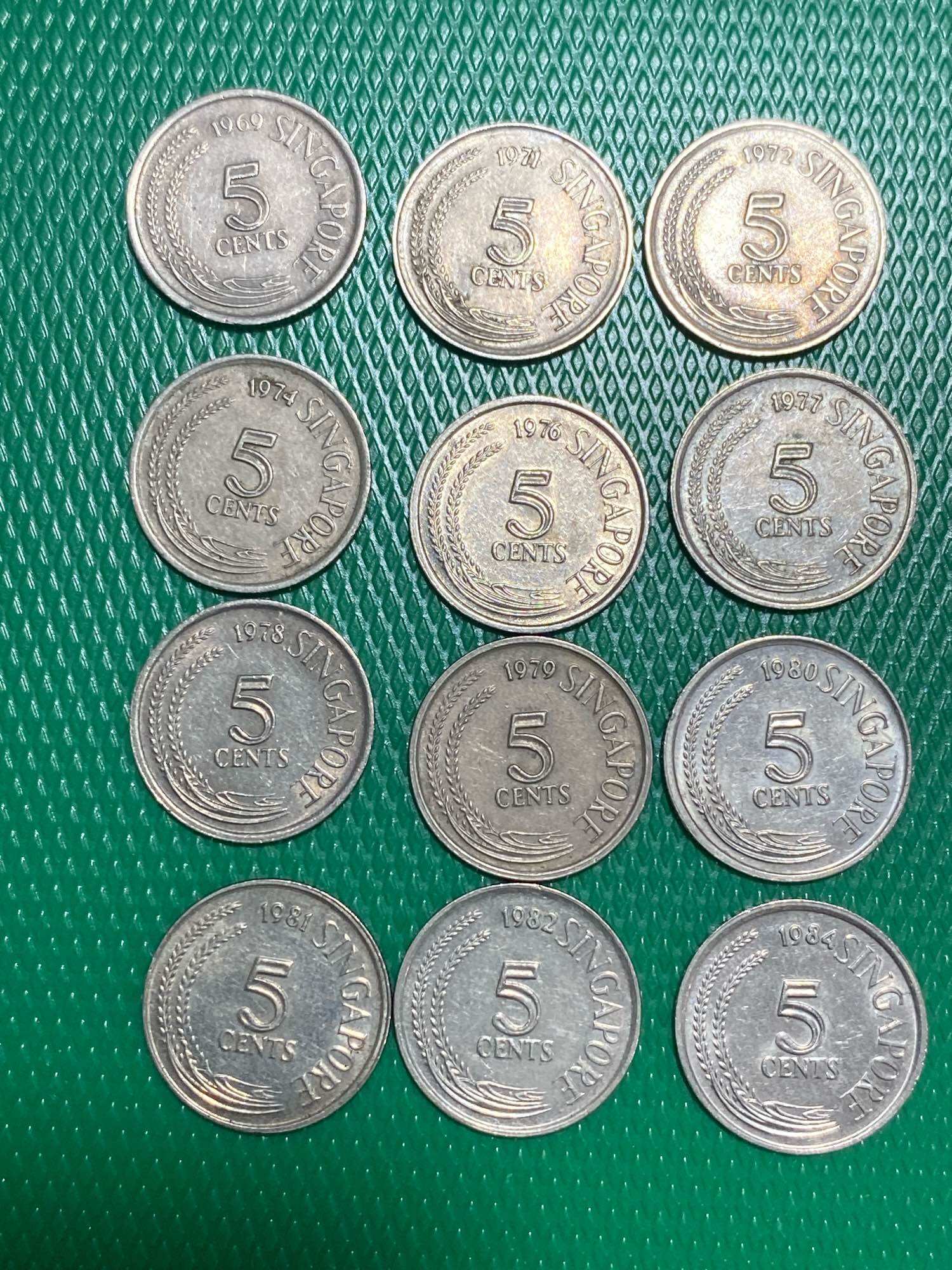 12 pcs Singapore 5 cents coins from 1969-1984 displayed on green surface. Silver coins with bird design.